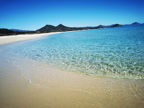 A beach with clear water, sandy shore, and mountains in the background. - Villasimius City Center (Villasimius)