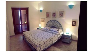 Une chambre à coucher avec un lit, deux tables de chevet avec des lampes, une porte et des cadres photos accrochés au mur.