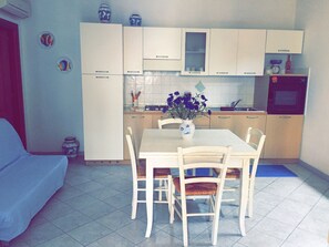 A compact kitchen with white cabinets, a dining table with chairs, and a small oven.
