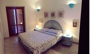 A bedroom with a bed, two bedside tables with lamps, a door, and wall-mounted picture frames.