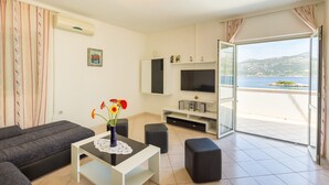 A modern living room with a sofa, a coffee table with a vase of flowers, a flat-screen TV, and a balcony with a view of the sea. - Vacation that you'll remember for a long time :) (Korcula)