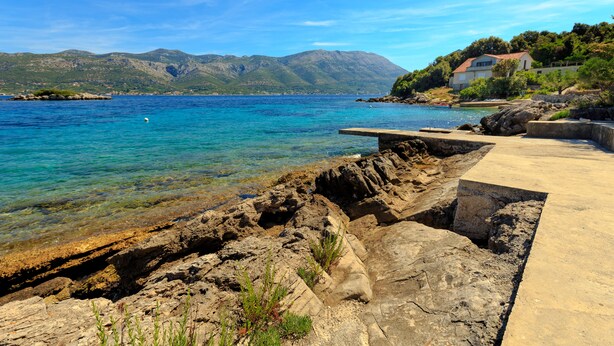 A coastal scene with clear blue waters, rocky shoreline, and a house on a hillside. - Vacation that you'll remember for a long time :) (Korcula)