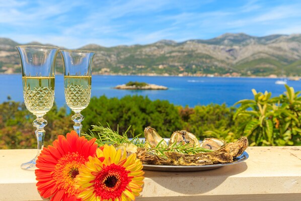 A table with two glasses of white wine, a plate of oysters, and a red and yellow flower.