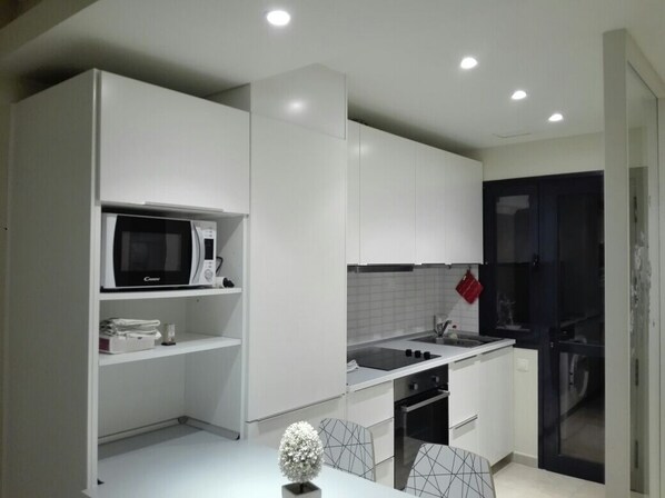 A modern kitchen with white cabinets, a microwave, a sink, and a small dining area with a table and chairs. - ocean view residence (Caleta De Fuste)