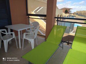 A balcony with a table and chairs, a green sun lounger, and a view of a swimming pool and buildings. - ocean view residence (Caleta De Fuste)