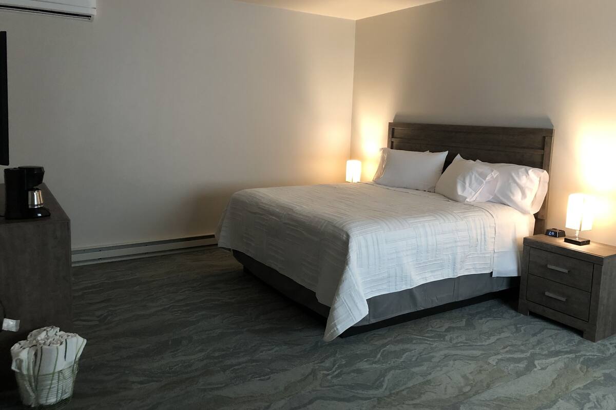 A hotel room with a bed, bedside tables, a coffee maker, and an air conditioning unit.