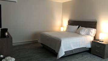 A hotel room with a bed, bedside tables, a coffee maker, and an air conditioning unit.