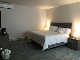 A hotel room with a bed, bedside tables, a coffee maker, and an air conditioning unit.