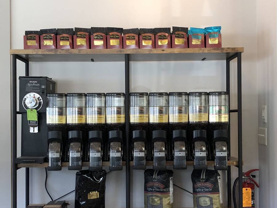 A coffee station with multiple coffee makers, bags of coffee, and a coffee grinder.
