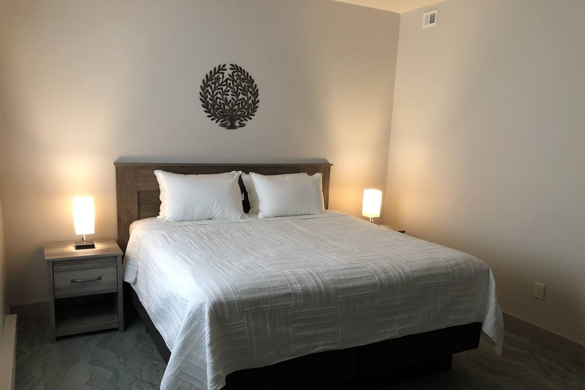 A neatly made bed with white linens, two bedside tables with lamps, and a wall-mounted decorative piece.