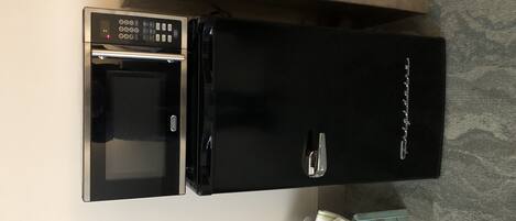 Un refrigerador negro con panel de control digital, un horno pequeño y un compartimento congelador.