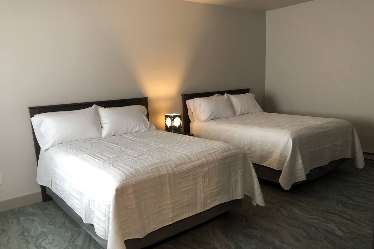 Two single beds with white bedding in a room with a marble floor and a nightstand with a lamp between them.