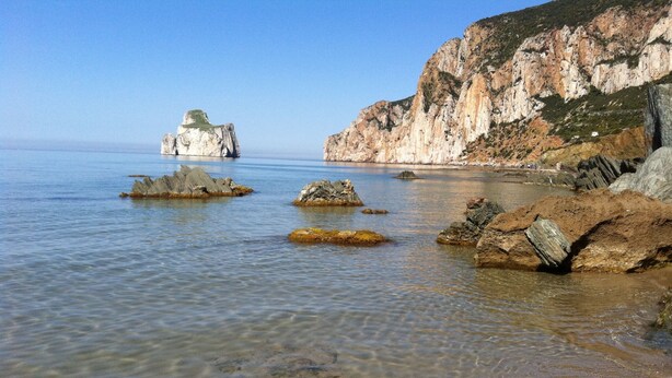 Paesaggio costiero con acque basse e trasparenti, affioramenti rocciosi e una scogliera.