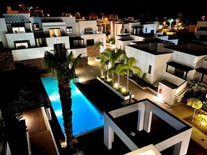 Un hôtel moderne composé de plusieurs bâtiments blancs, doté d’une piscine et bordé de palmiers.