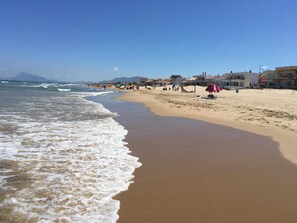Une plage avec un rivage sablonneux, des vagues et des bâtiments en arrière-plan.