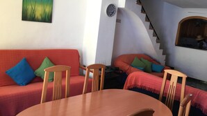 Ein gemütliches Zimmer mit einem roten Sofa, Holzstühlen, einem runden Tisch und einer Treppe, die in eine obere Ebene führt.