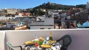 Eine Terrasse mit einem für zwei Personen gedeckten Tisch, mit Blick auf eine Stadtlandschaft mit Gebäuden und einer Hügelkette.