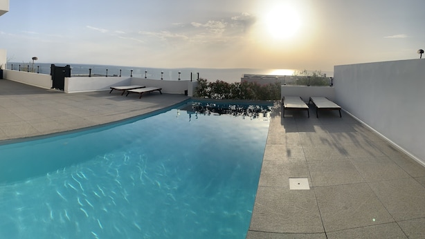 Une piscine sur le toit, avec une eau d’un bleu cristallin, entourée de murs blancs et agrémentée de quelques chaises longues.
