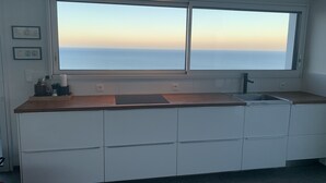 Une cuisine moderne dotée d’une grande fenêtre donnant sur la mer, de meubles blancs et d’un plan de travail avec un évier.