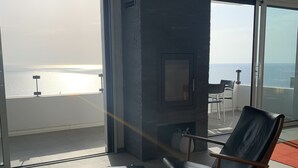 Un salon moderne doté d’une grande porte vitrée donnant sur un balcon avec vue sur la mer. On y trouve une table en bois et deux chaises.