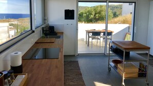 Une cuisine moderne avec vue sur la mer, un coin repas avec une table et des chaises, et une porte-fenêtre coulissante donnant sur un espace extérieur.