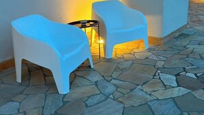 Two white plastic chairs with a small table between them, set on a stone-paved patio with a wall in the background. - Tenuta Gli Agrumi del Salento (Carmiano)