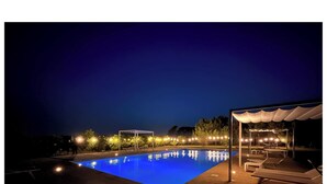 A nighttime swimming pool with a clear blue surface, surrounded by lounge chairs and a covered seating area. - Tenuta Gli Agrumi del Salento (Carmiano)