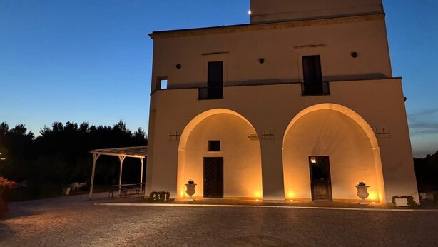 A building with a central entrance flanked by two arches, a flat roof, and a small balcony on the upper level. - Tenuta Gli Agrumi del Salento (Carmiano)