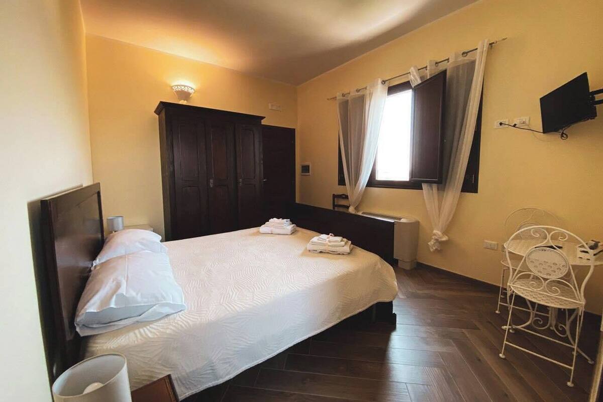 Un dormitorio con cama, una silla, un televisor y una ventana con cortinas.