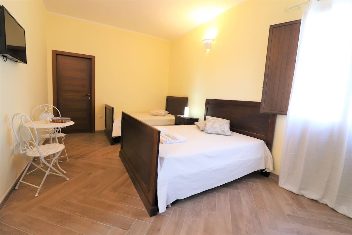 Una habitación de hotel con una cama, una pequeña mesa con sillas, un televisor en la pared y una puerta.