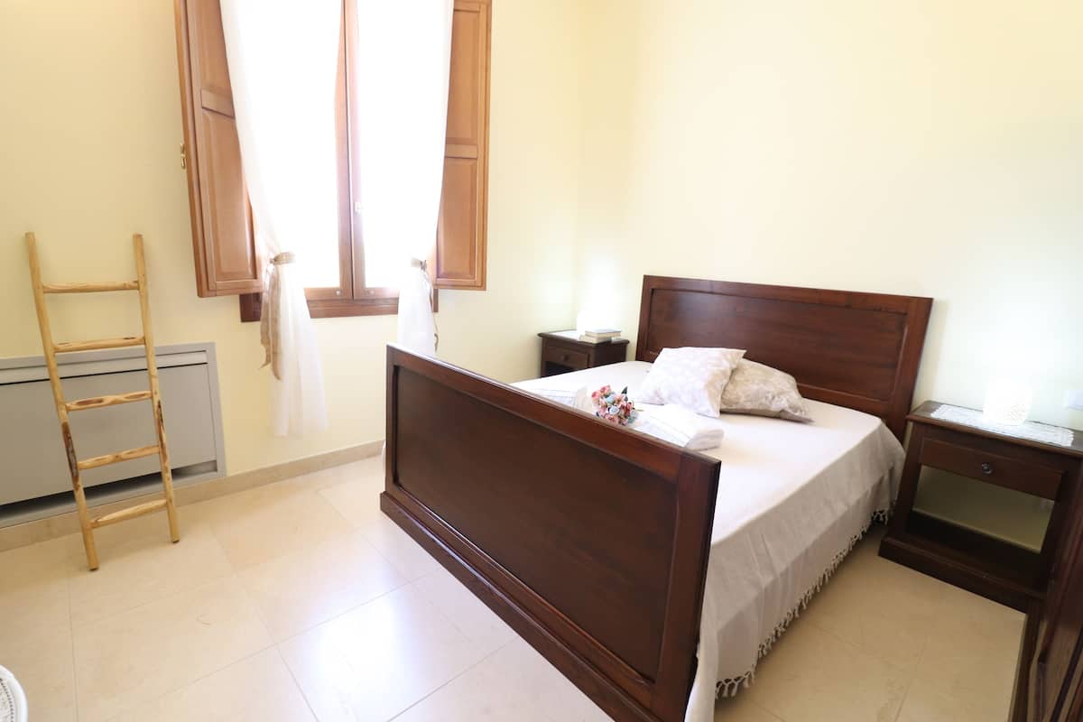 Un dormitorio con cama de madera, mesita de noche, escalera y ventana con cortinas.