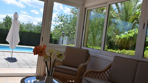 A sunlit room with a view of a swimming pool, wicker furniture, and a vase with flowers. - CAN LA (Wi-Fi Villa) (Pollensa)