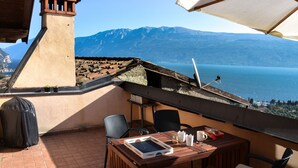 A terrace with a table, chairs, and a view of a lake and mountains.