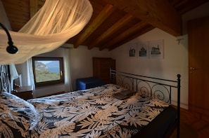 A bedroom with a bed, a window with a view, a wooden ceiling, and a door.