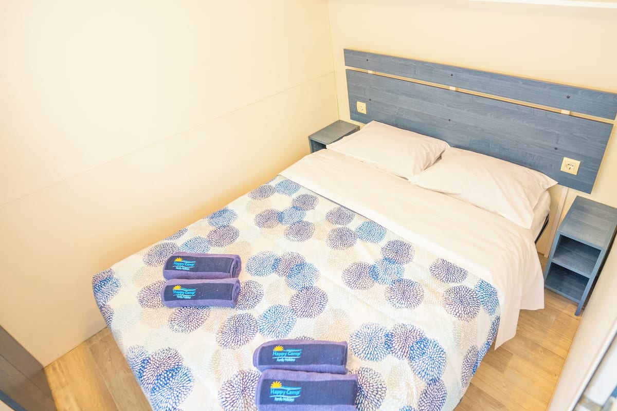 A neatly made bed with a patterned bedspread, two pillows, and two folded towels on the bed.