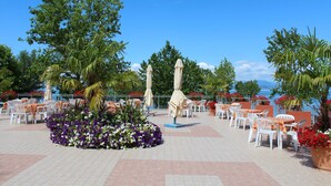 Un área de patio al aire libre con mesas y sillas, rodeada de plantas y sombrillas.