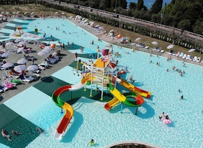 Une grande piscine extérieure dotée de plusieurs toboggans et de transats.