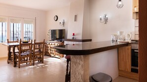 Una cocina moderna con una isla central, sillas de madera, una mesa de comedor, un televisor y una cafetera.