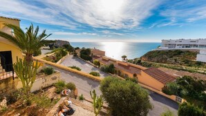 Zona residencial costera con edificios de estilo mediterráneo, una calle pavimentada y vista despejada al mar.