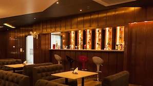 A bar area with wooden paneling, multiple seating options, and a variety of bottles and glasses on shelves. - Hotel RG Inn (Jaipur)