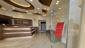 A hotel reception area with a wooden reception desk, a glass wall, and a red sign. - Hotel RG Inn (Jaipur)