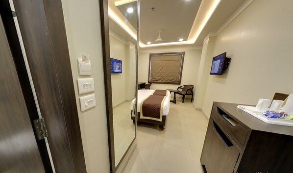 A hotel room with a bed, bedside table, chair, TV, and a desk with a computer.