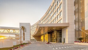 Un hôtel moderne à la façade incurvée, doté de grandes fenêtres et d’un hall d’entrée bien entretenu agrémenté de parterres de fleurs.