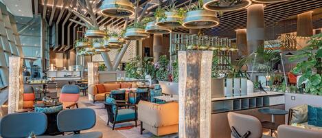A modern interior with high ceilings, hanging planters, and a variety of seating arrangements.