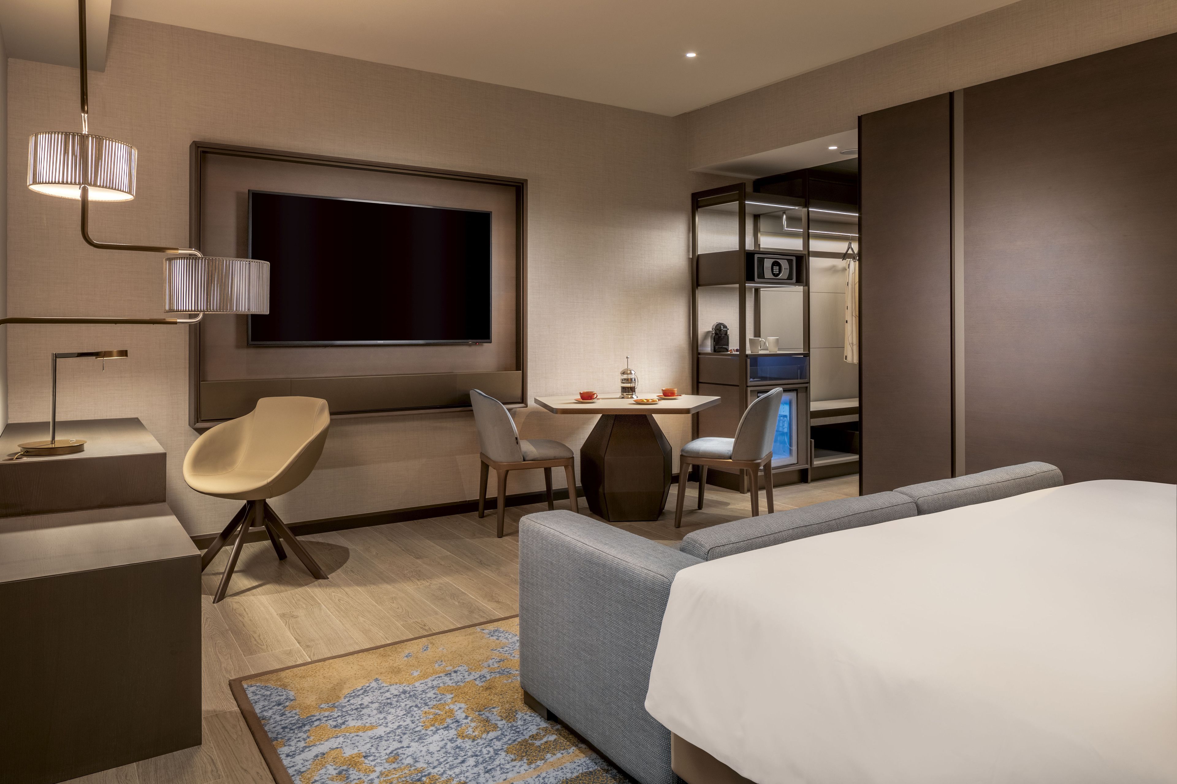 Habitación de hotel moderna con una cama grande, un escritorio con silla, un televisor montado en la pared y un armario.