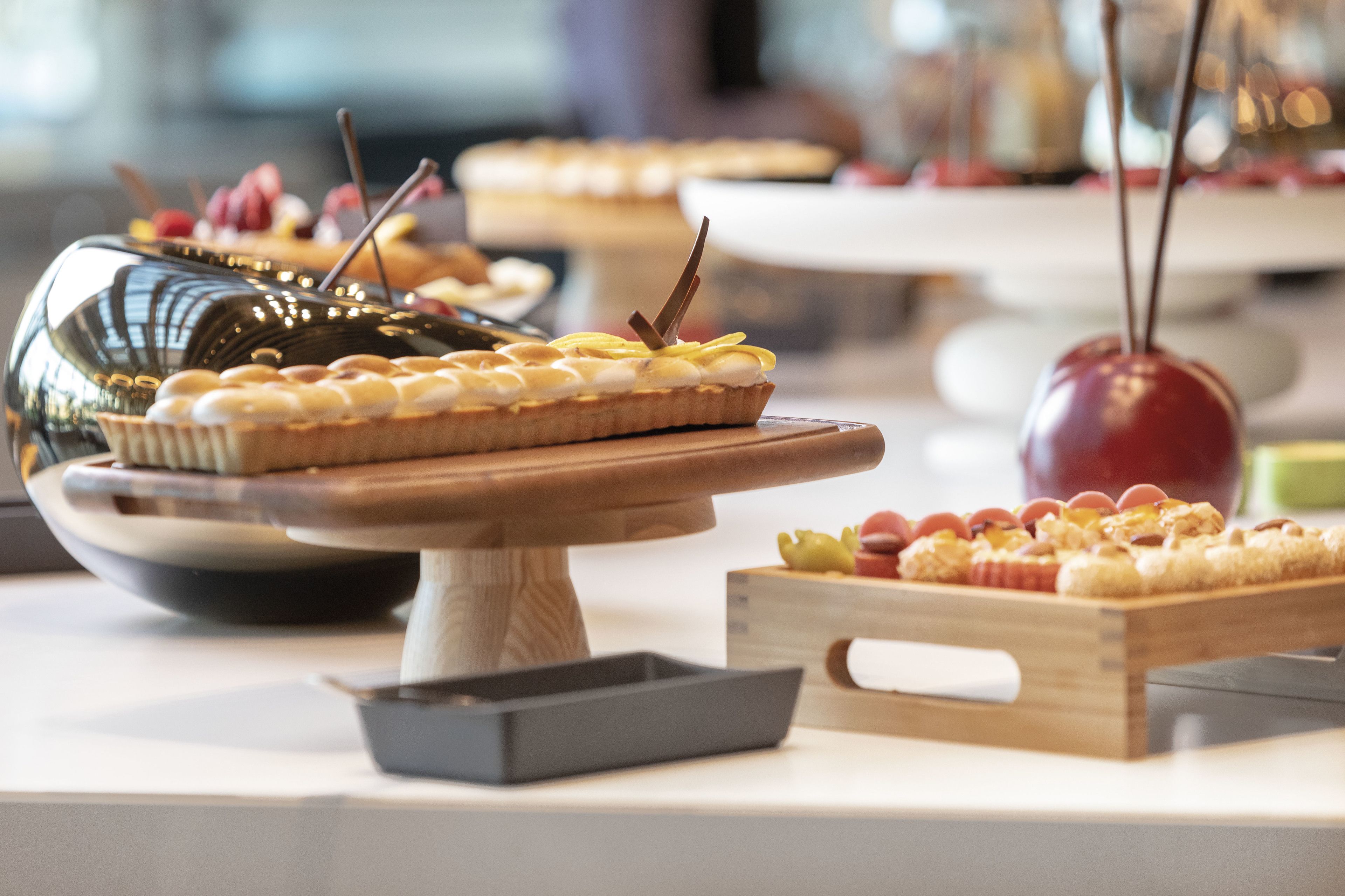 Variedad de postres a la vista, incluyendo pasteles y dulces, colocados sobre soportes de madera y una bandeja metálica.