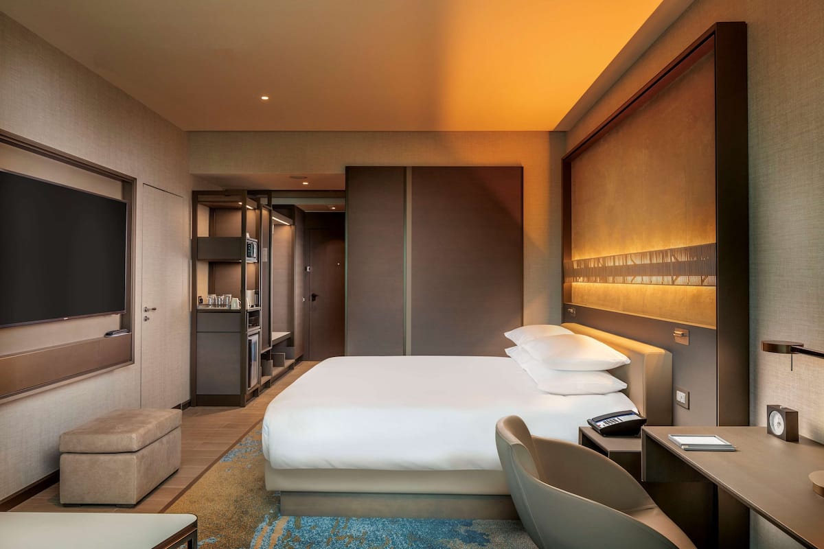Une chambre d’hôtel comprenant un lit, une table de chevet, une chaise, un bureau et un téléviseur.