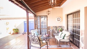 An outdoor patio area with two chairs and a table, a stone wall, and a wooden ceiling.