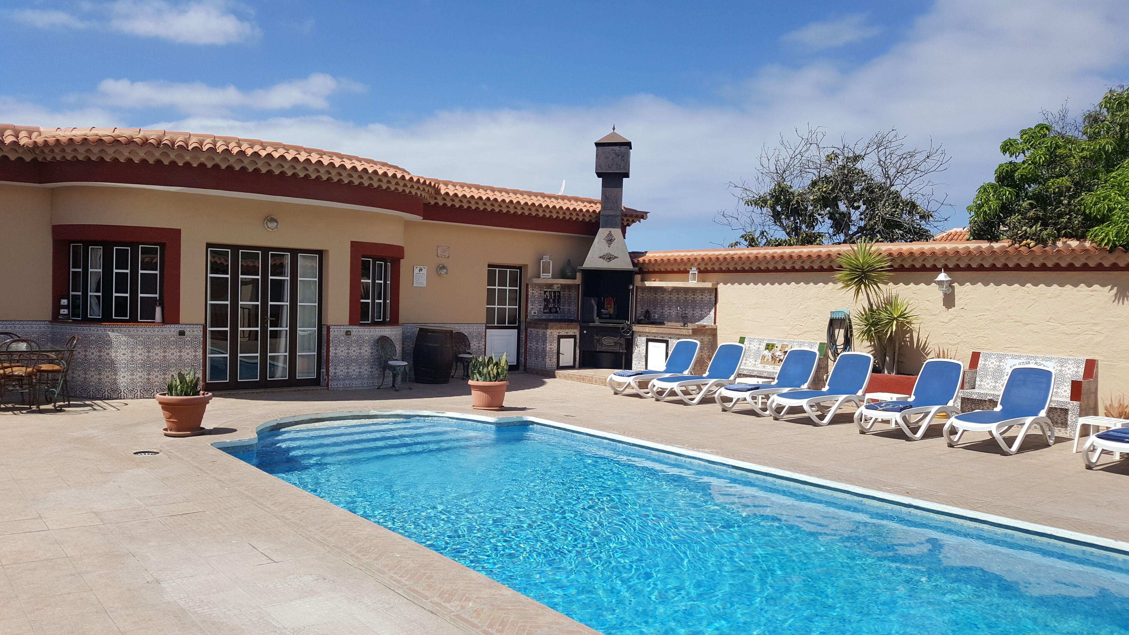A swimming pool with lounge chairs, a patio area, and a building with a tiled roof and decorative walls.