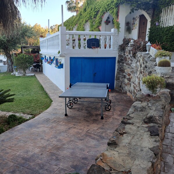 Una mesa de ping pong en un espacio exterior con un muro de piedra y una puerta azul.